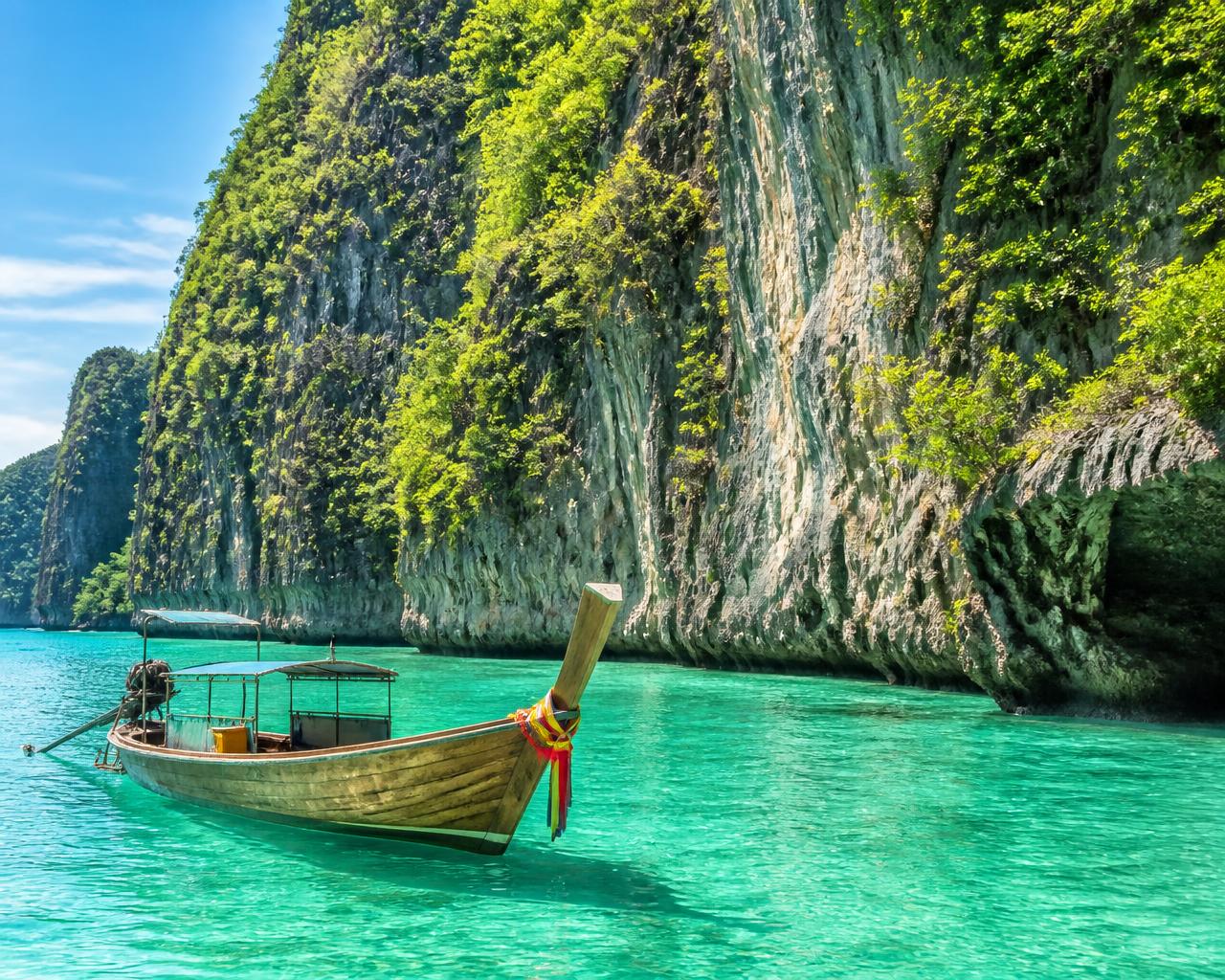 A longtail boat on clear emerald water beside limestone cliffs in Thailand